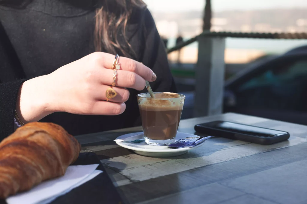 young-caucasian-woman-talking-by-phone-while-taking-coffee-croisant-terrace